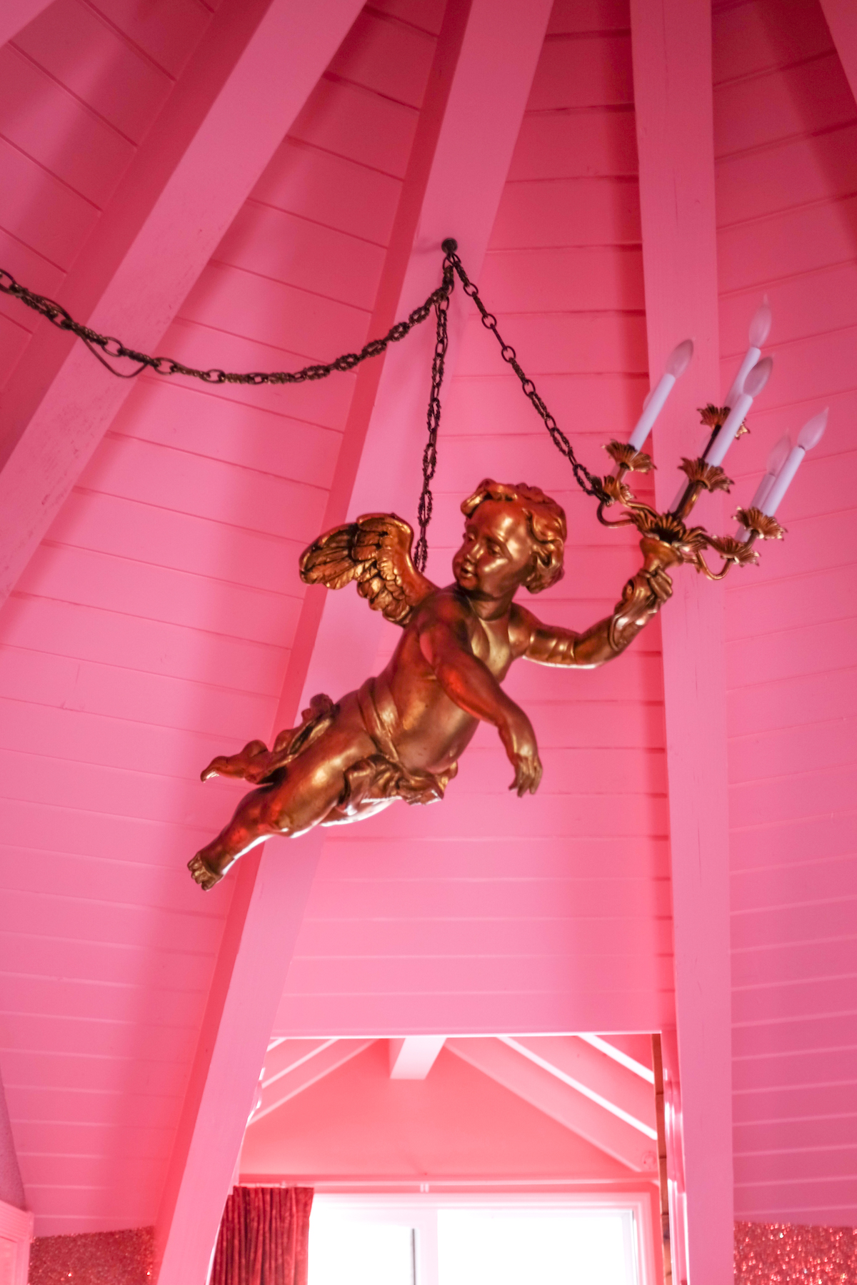 Gold cherub chandelier hanging from bubblegum pink vaulted ceiling in a room at the Madonna Inn.